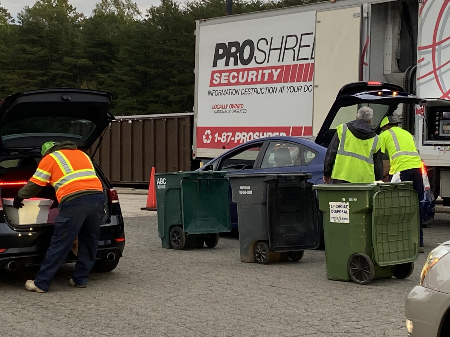Workers taking boxes of paper out car trunk for shred event. 